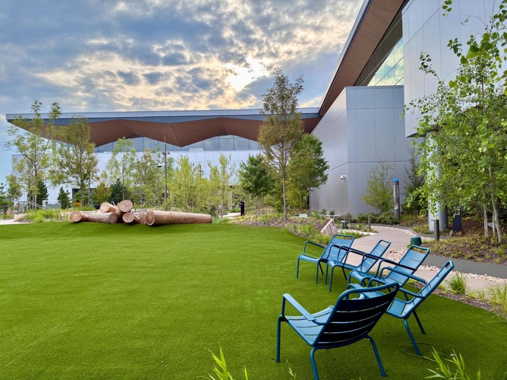 A landscaped outdoor space featuring picnic chairs and trees beneath a cloudy sky with the sun setting.