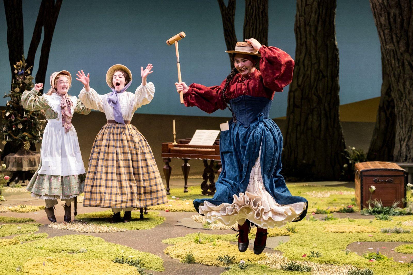 Three people dancing and singing in costume on a stage.