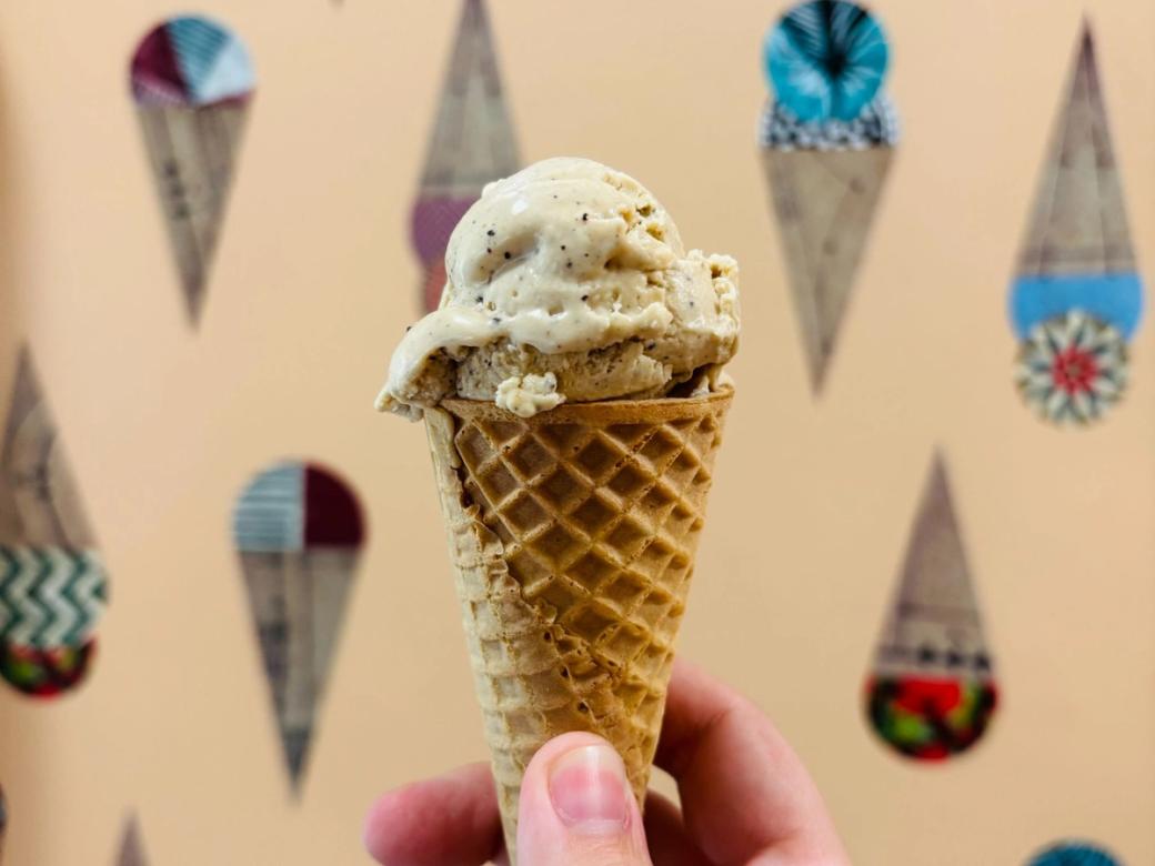 Closeup of a hand holding a vanilla ice cream. Geometric ice cream wallpaper in the background.