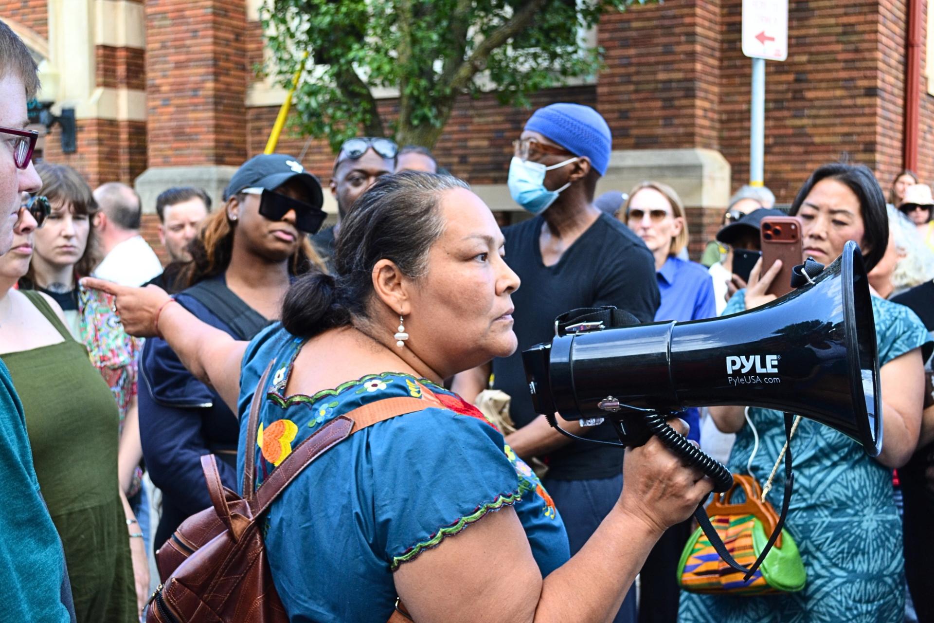 A woman in a blue dress points in the middle of a crowd.