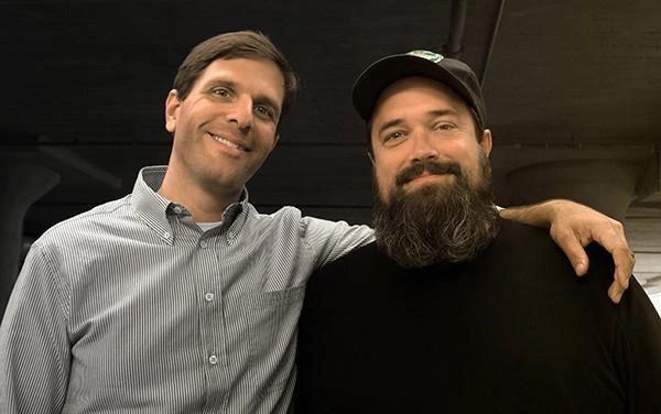 Two men, one in a gray-button down and one in a black sweater.