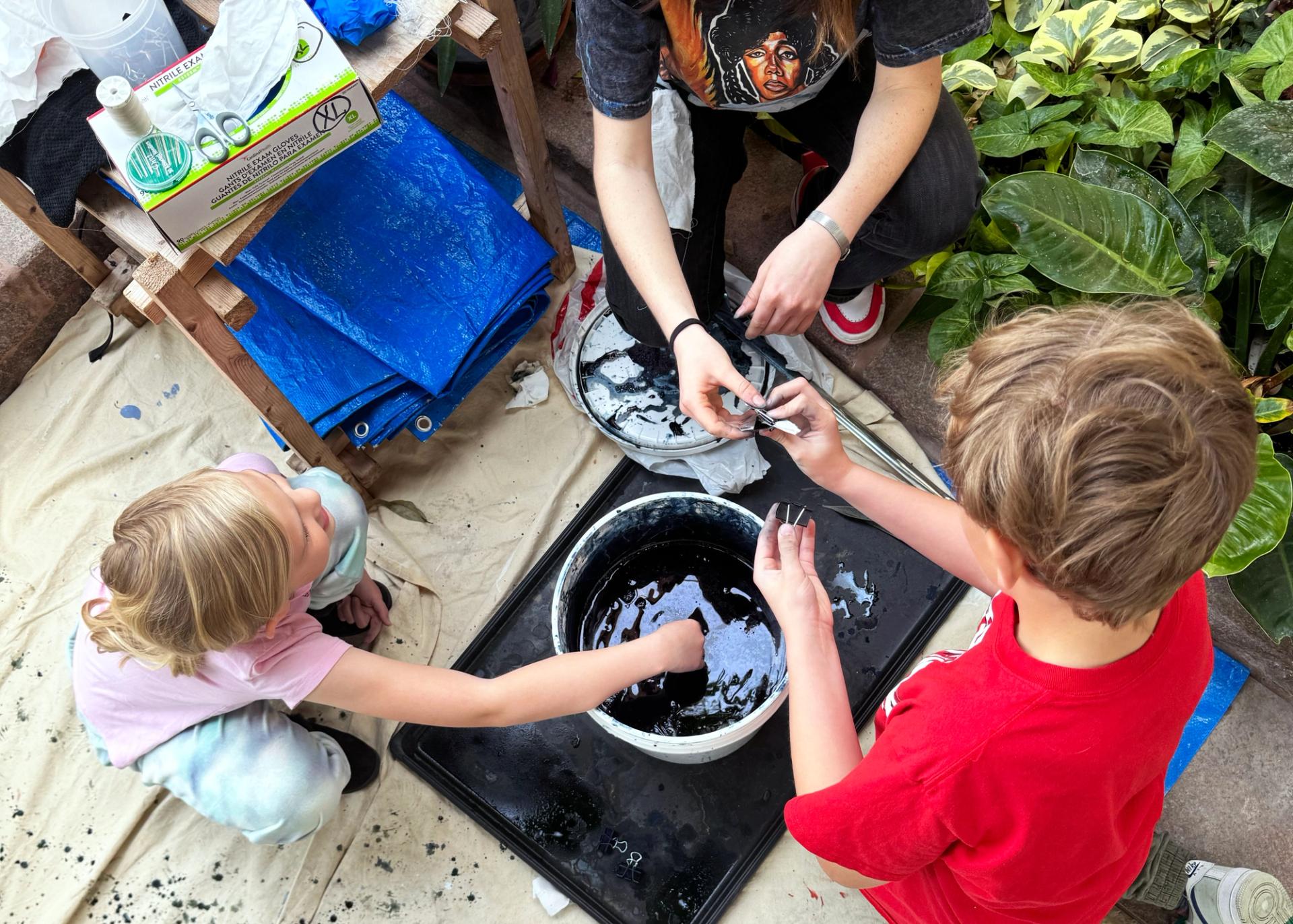 Three children play with a bucket of blue dye.