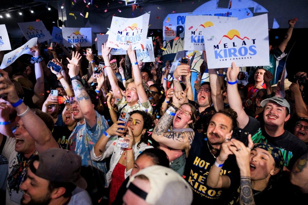 A large crowd of people cheering and holding up signs that say "Melat Kiros for Congress." Confetti is falling behind and around them.