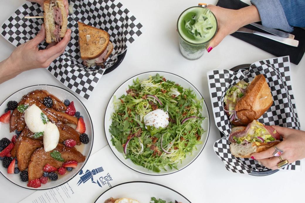 A salad and french toast on two separate plates. People's hands can be seen grabbing sandwiches. 