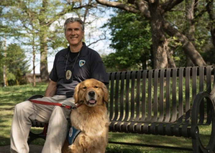 A police officer sits on a bench next to a golden retriever.