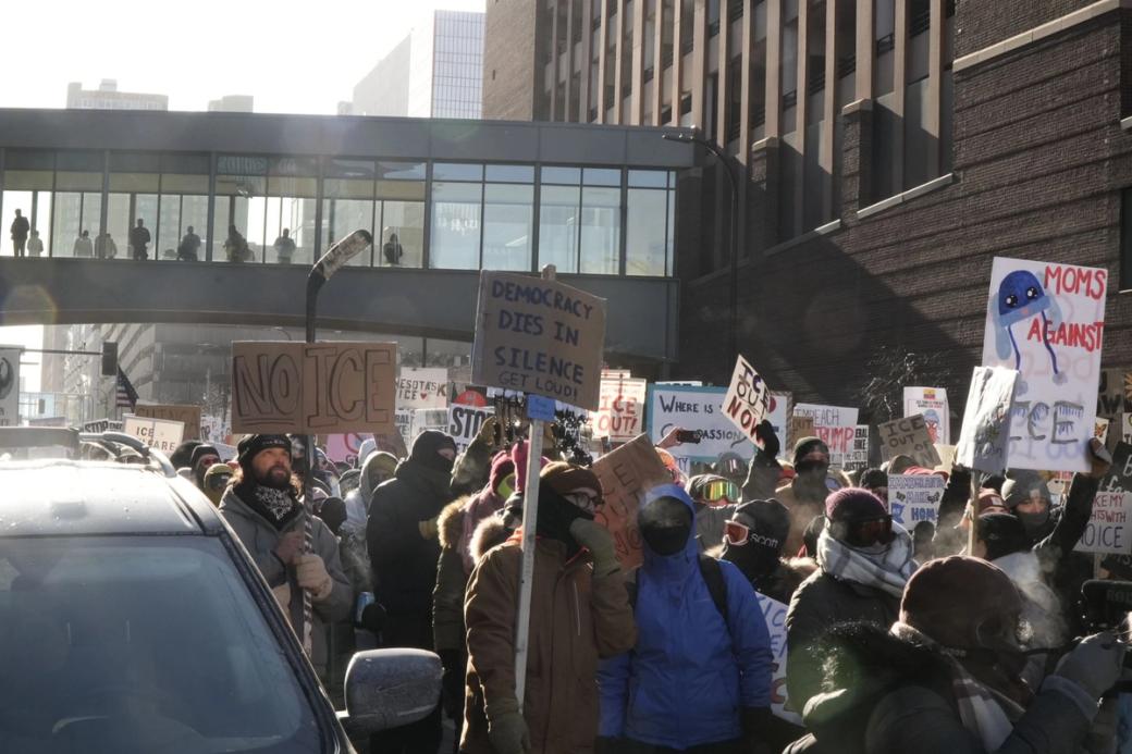 Protestors holding signs marching in large group down urban street