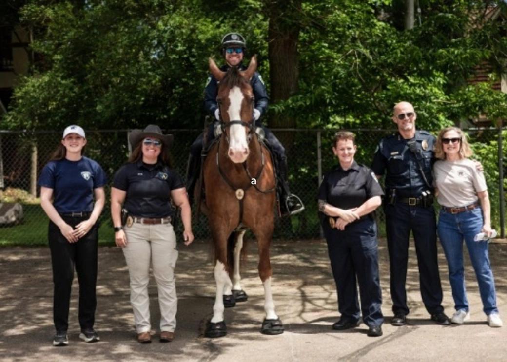 A group of Madison police officers stand smiling. One officer sits on a horse.