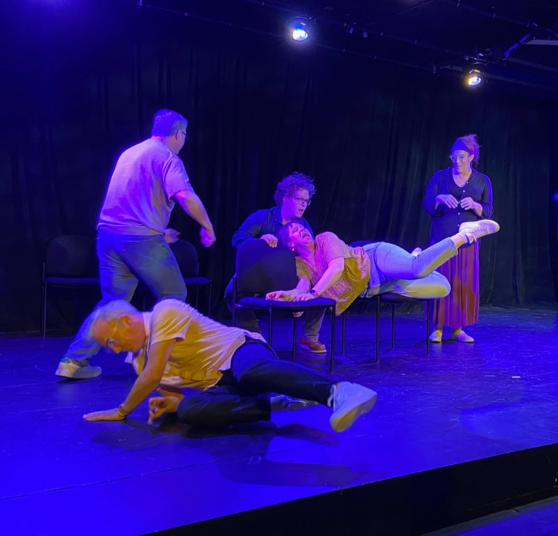 Four people on a stage, three are standing, two seem to be falling