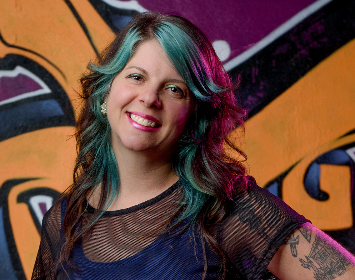 Woman with green highlights, standing in front of orange-and-blue street art, Portland, Oregon