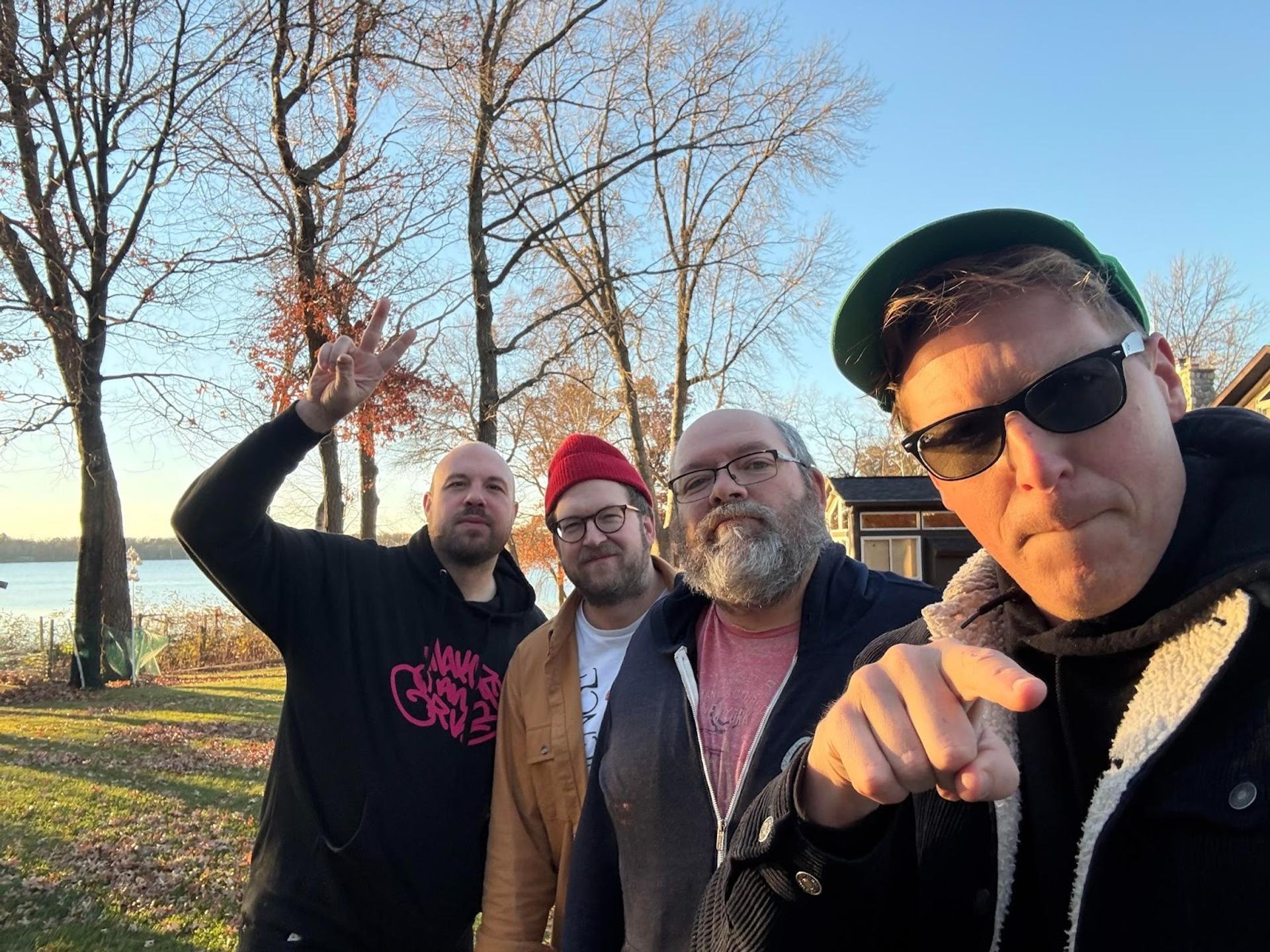 Four men taking a selfie together in a field on a sunny day
