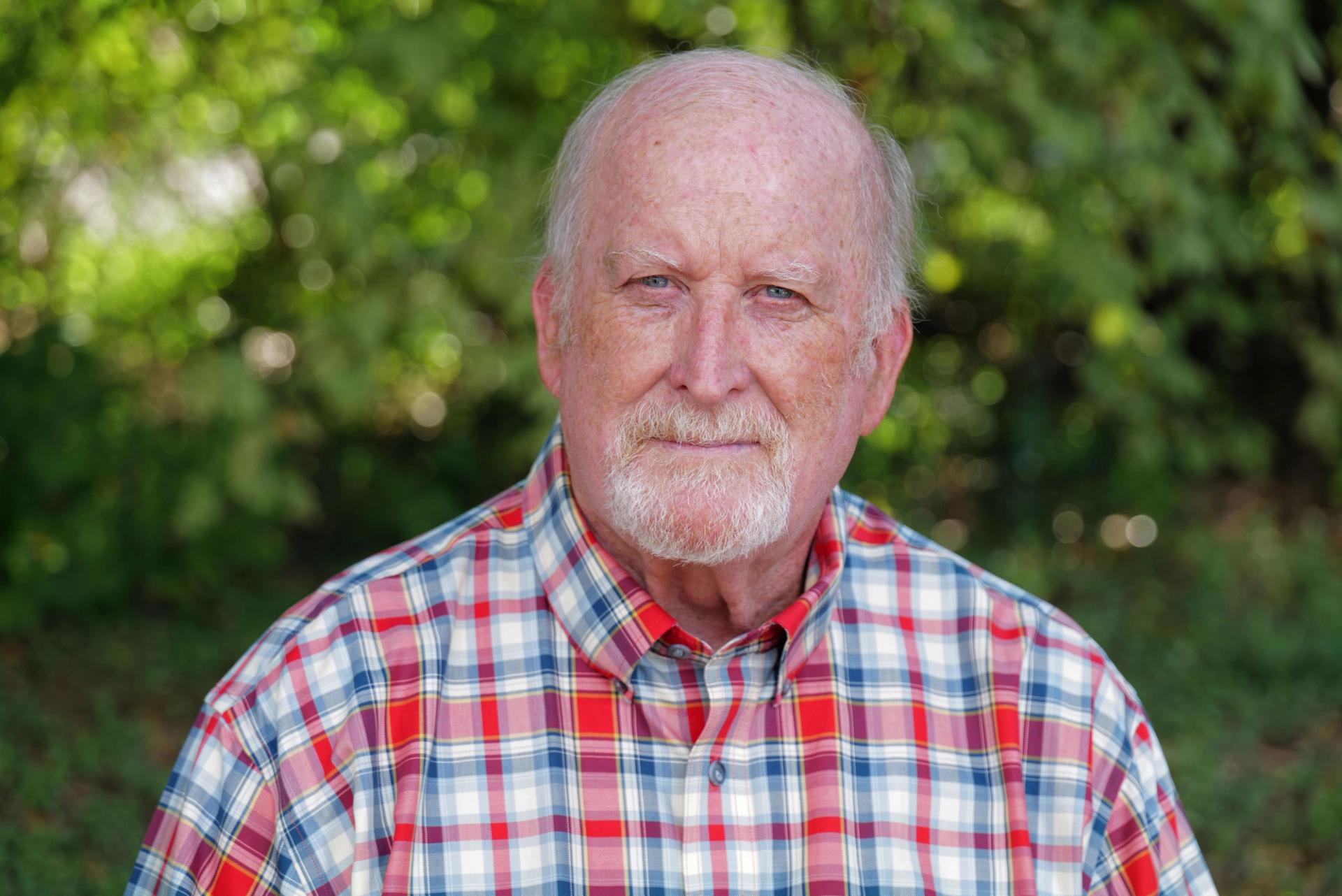 A photo of a man wearing a red, white, and blue plaid button-down shirt.