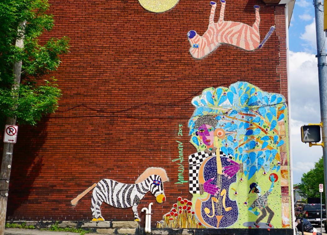 a mosaic mural on a red brick building of a zebra, bass player, and skateboarder