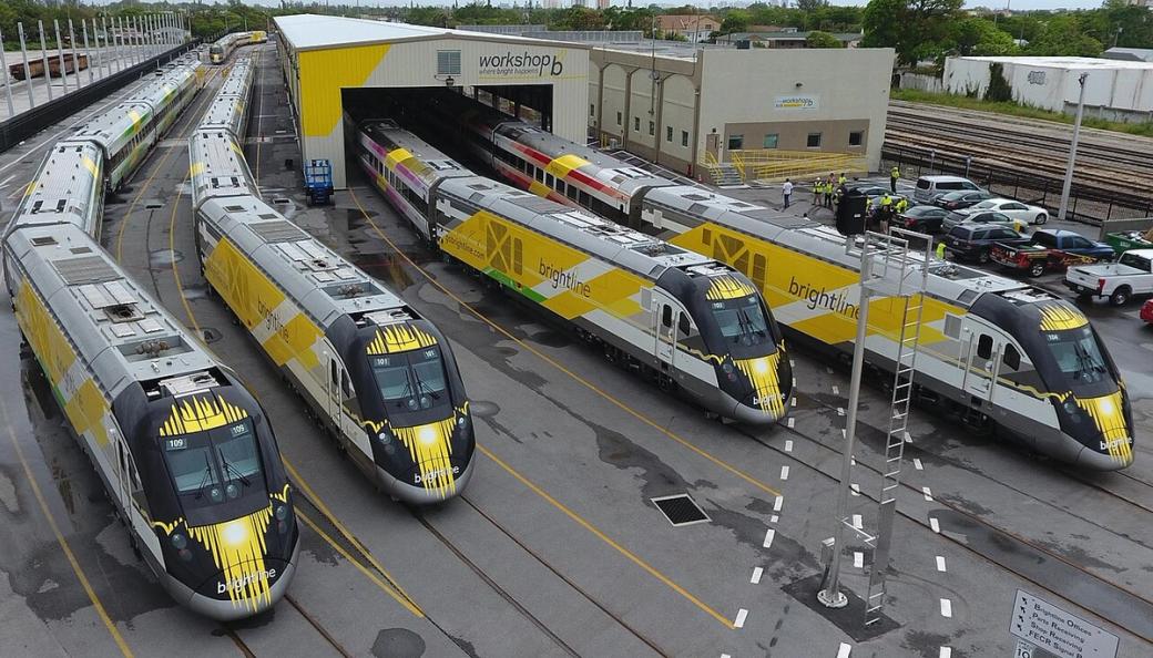 A row of yellow, black and silver trains in a train yard.