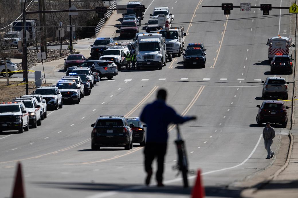Sillhouette of a man walking a bike on a busy street while many emergency vehicles line the street