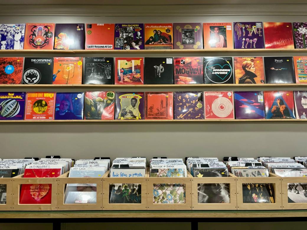 three shelves of orange, black, and purple colored records above a table of record boxes