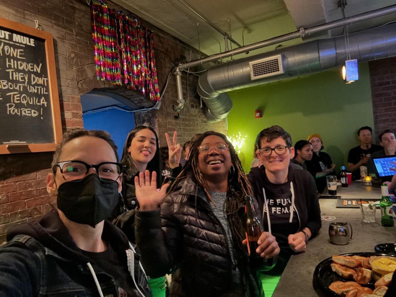 Several people waving at the camera in a bar.