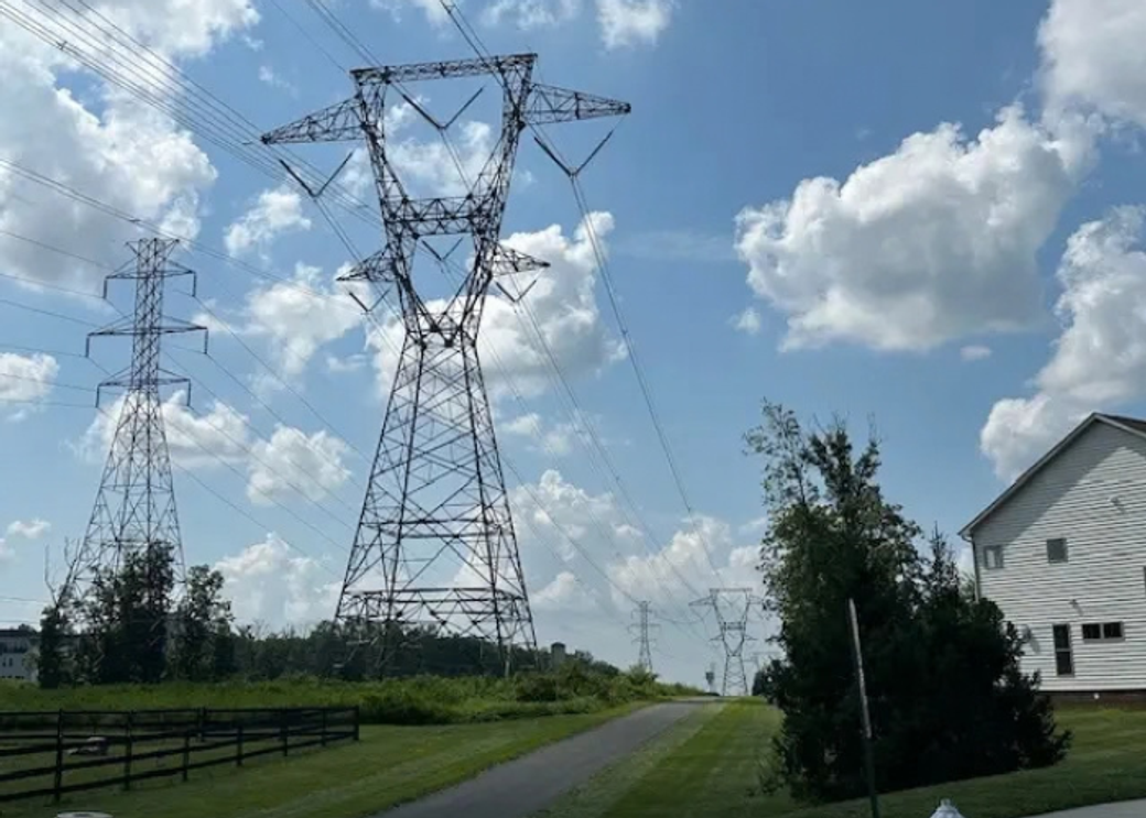 Two electrical towers sit close to a white house.