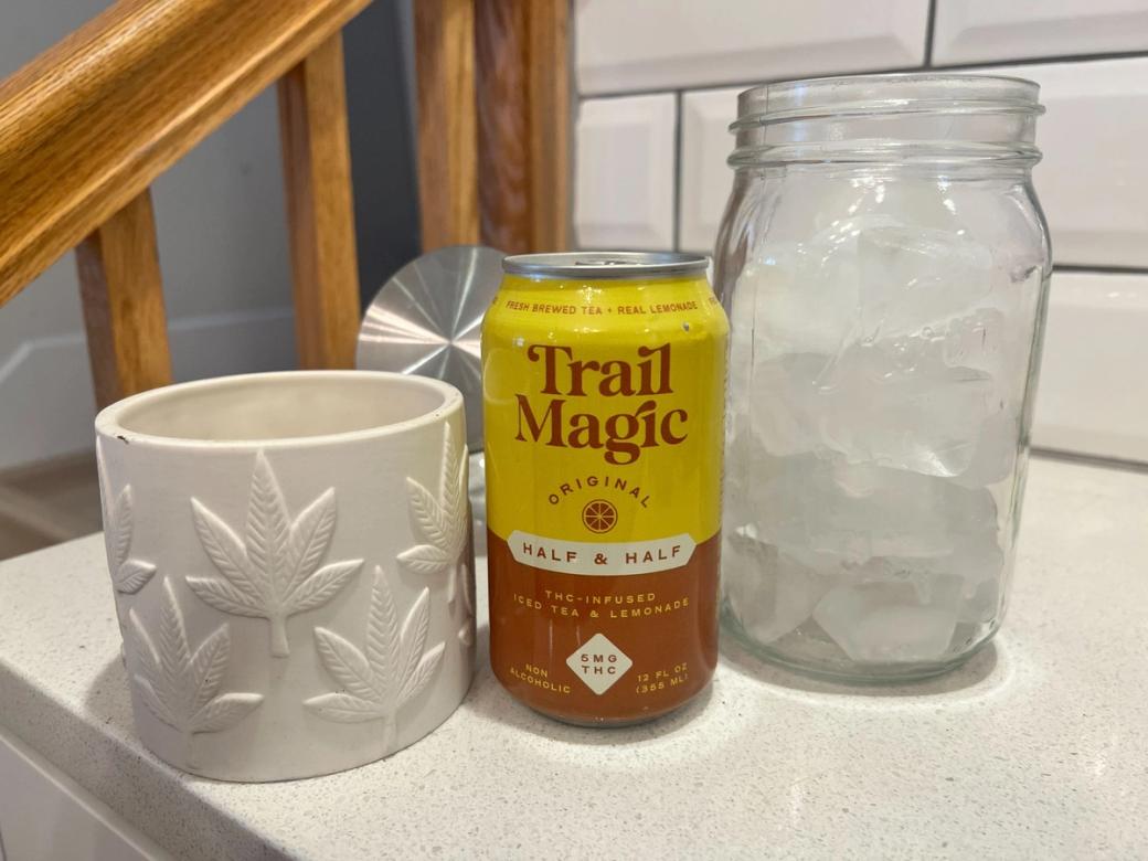 Yellow and brown can of THC infused brewed tea, with one mug and one ice-filled jar sitting next to it on white kitchen counter