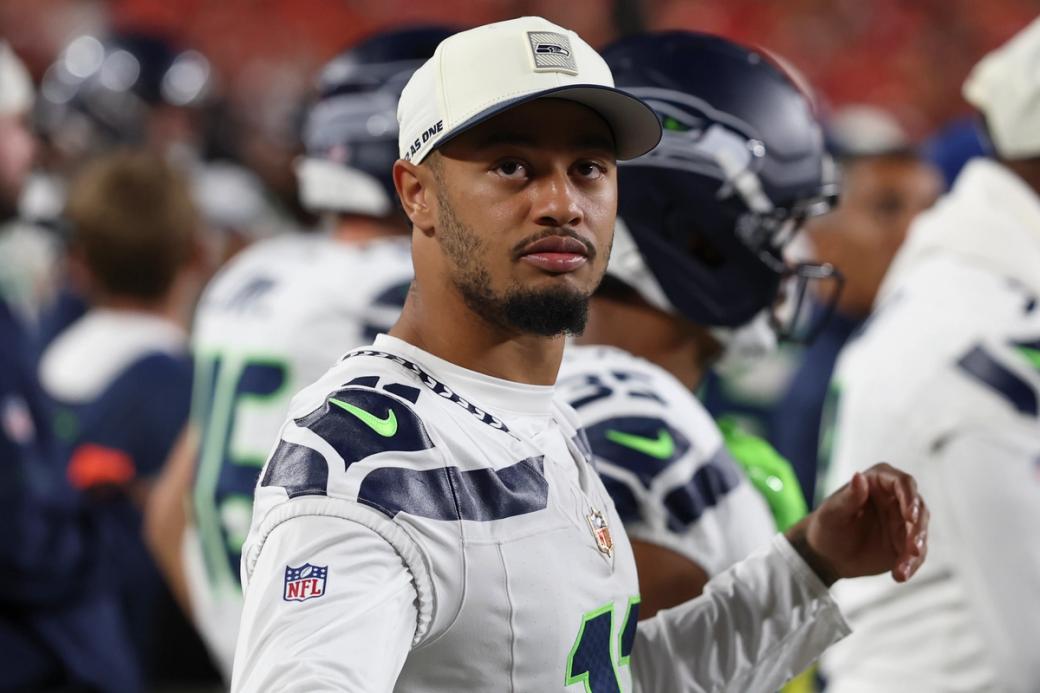 An image of Jaxon Smith-Njigba in a baseball hat on the sidelines of a preseason game