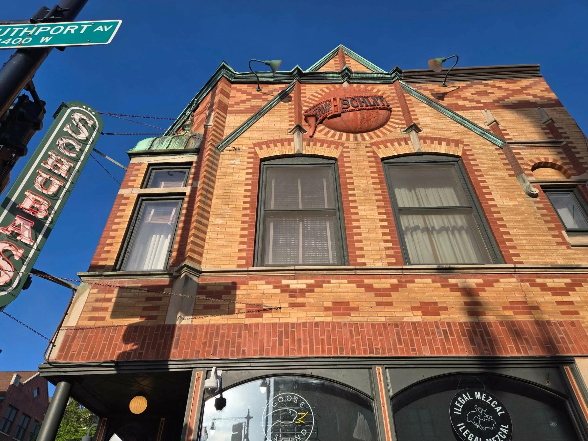 A pedestrian view facing up at a brick building. A sign on the left says "Schubas"