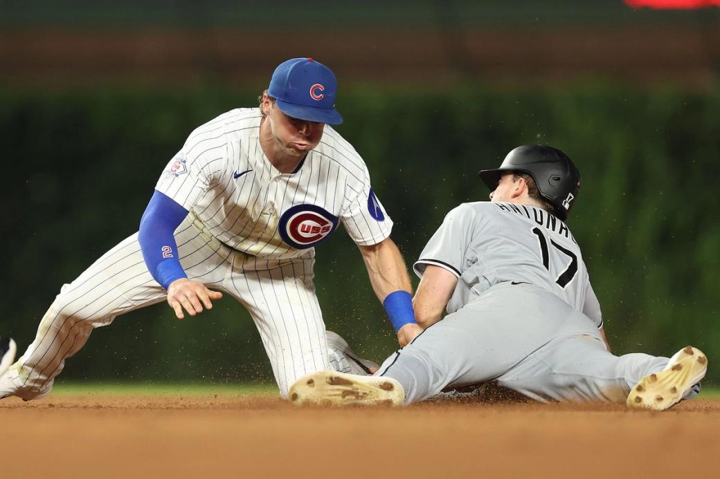 A man in a cubs uniform bracing for a man in a white sox stealing a base
