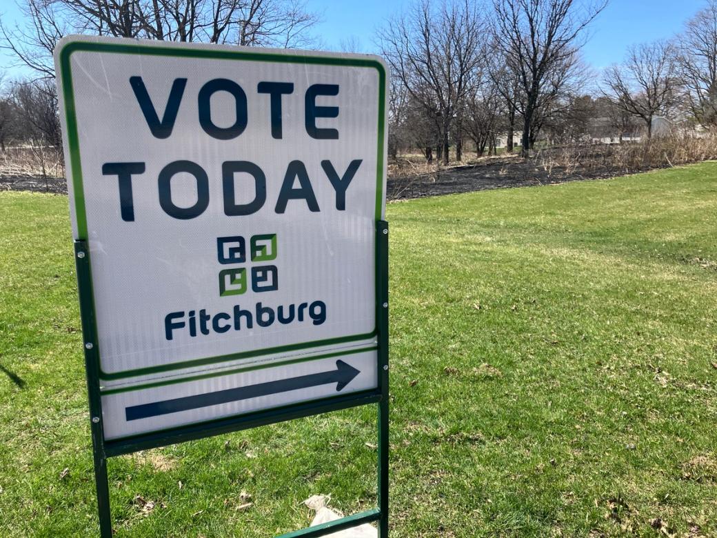 A white sign with an arrow in a grassy field.