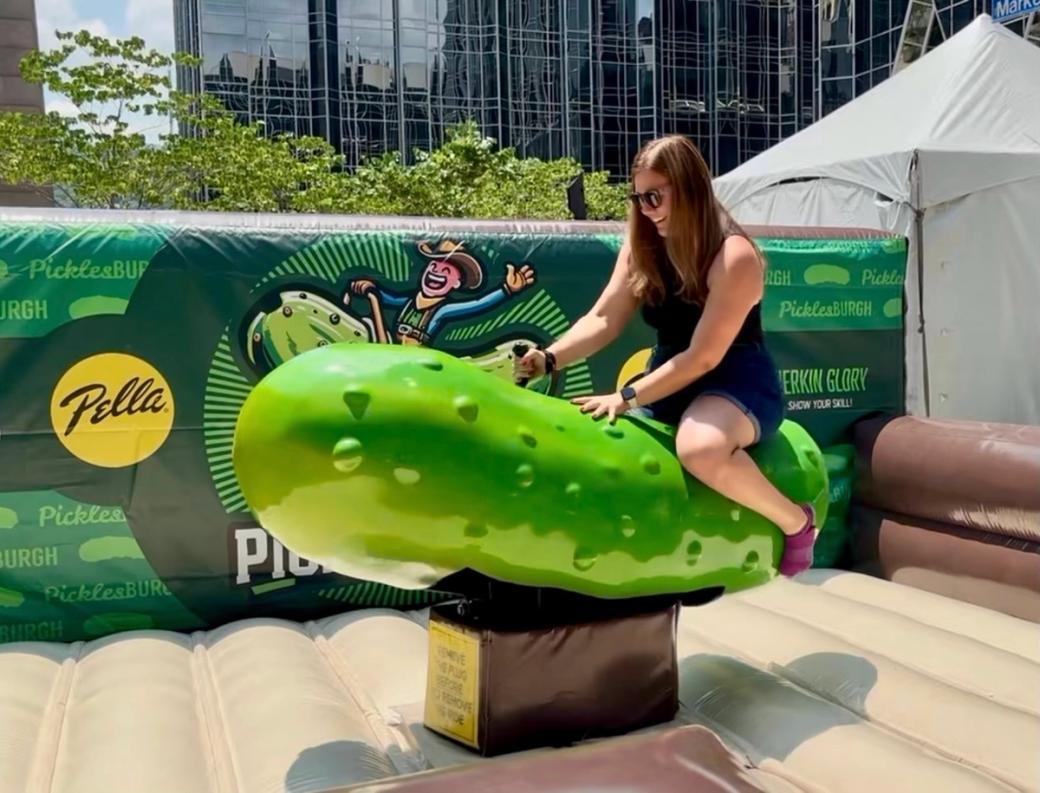 Megan Harris sits on a bright green mechanical pickle, the Picklesburgh equivalent to a mechanical bull.