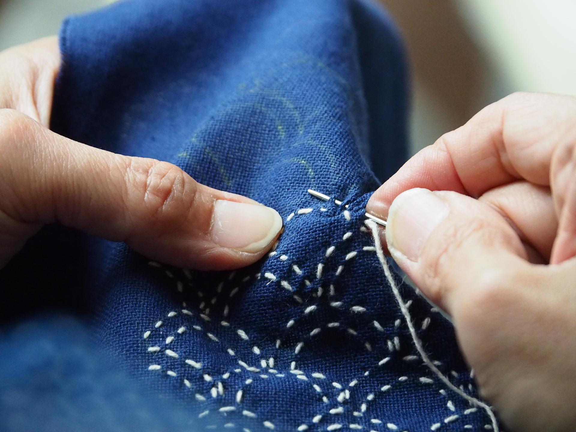Closeup of person sewing indigo fabric with white thread.