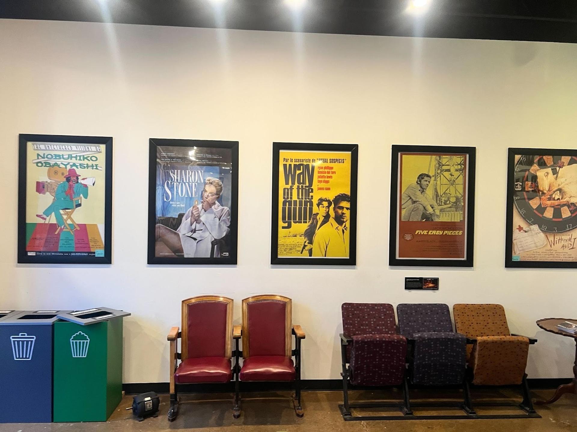 An arrangement of movie posters on the wall. There are old theater seats below of them as well