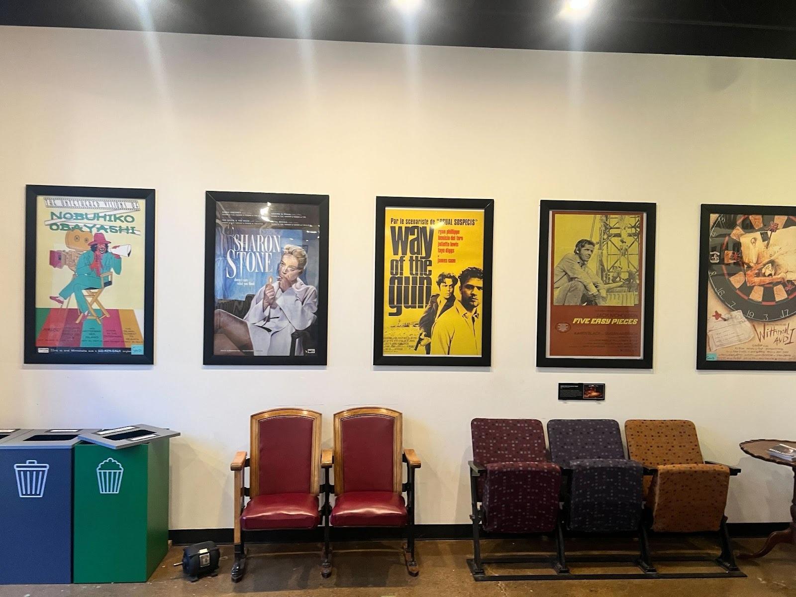 An arrangement of movie posters on the wall. There are old theater seats below of them as well