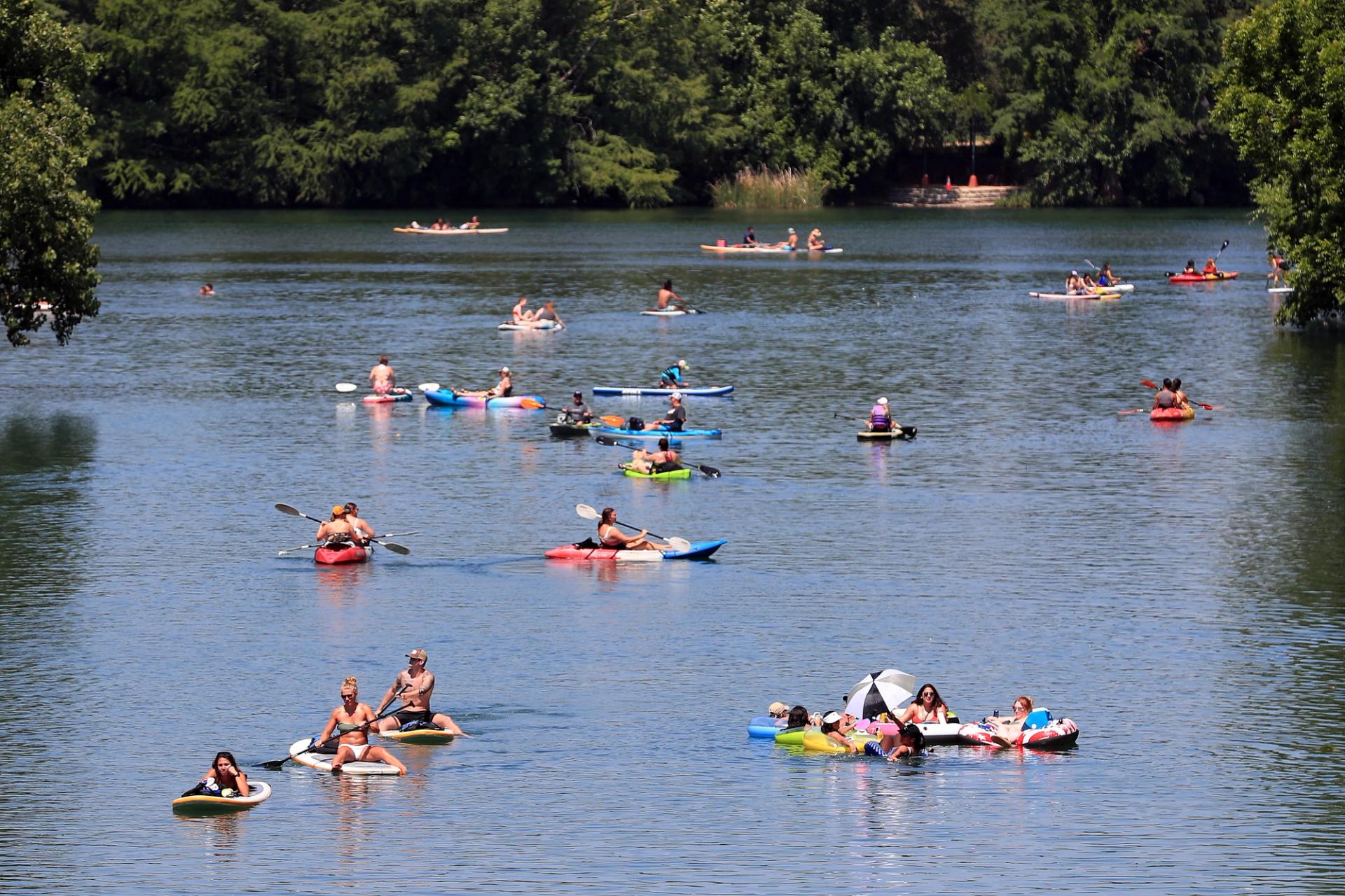 People kayak and paddle board in a large lake that is a dark blue color.