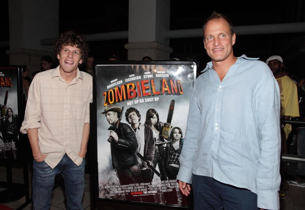 Jesse Eisenberg and Woody Harrelson in front of a "Zombieland" movie poster.