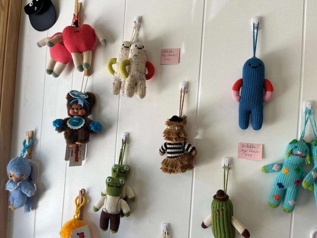 Colorful knitted bag charms made to look like various animals and characters hang on a wall