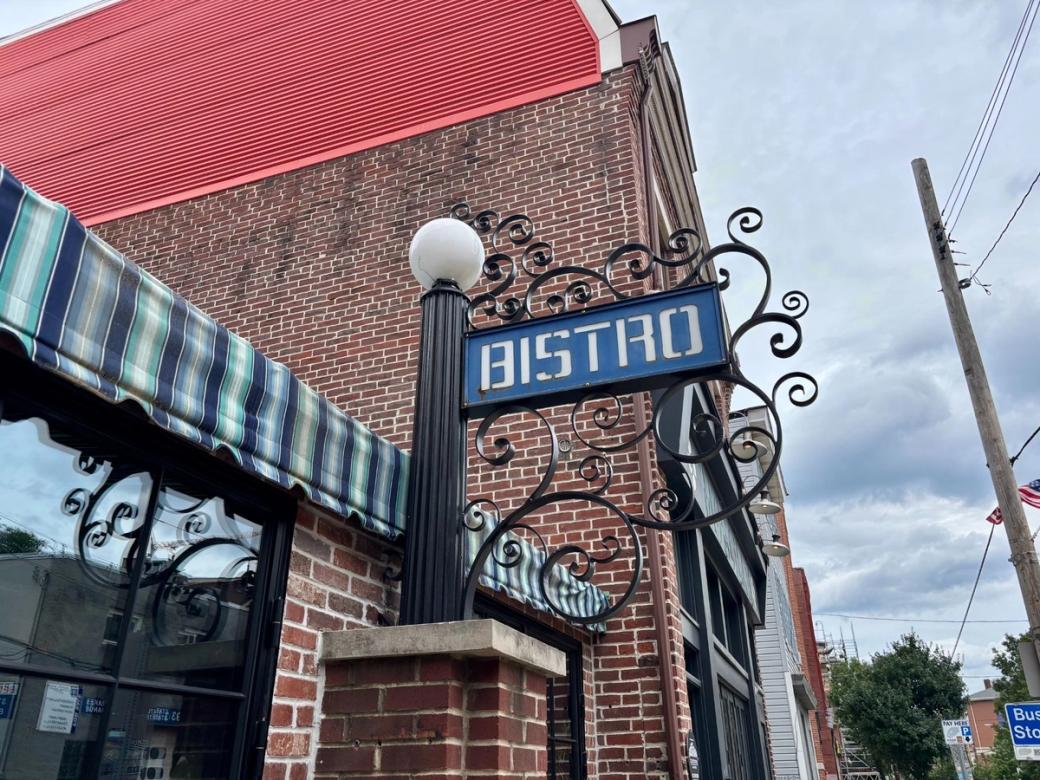 Sidewalk view of a brick building with a blue "BISTRO" sign and a red roof.