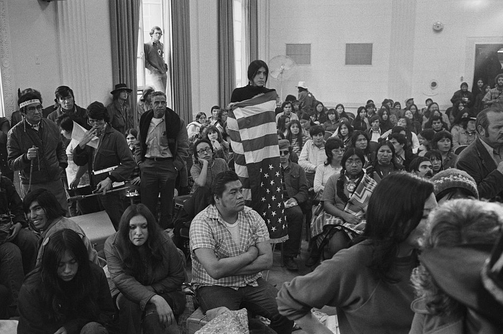 A Native American girl is wrapped in an upside down American flag as she and a group of about 500 Native Americans occupy an auditorium at the Bureau of Indian Affairs in November 1972. (Bettmann/Getty Images)