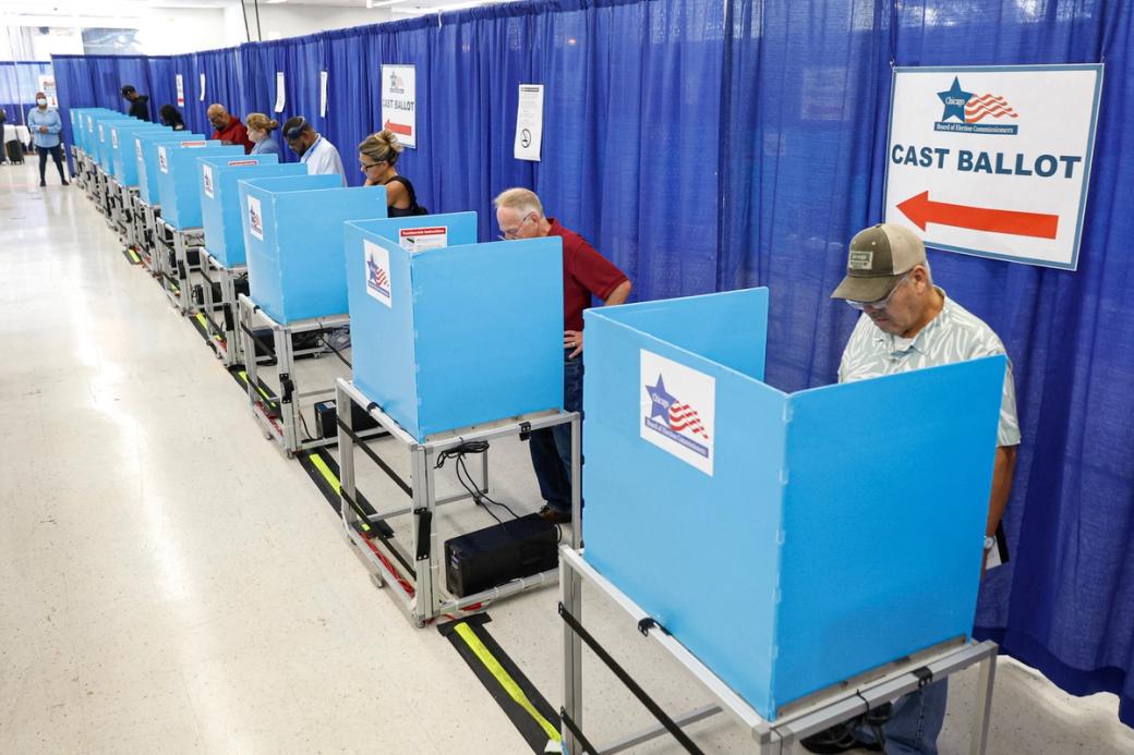 Line of voting booths filled with voters, and sign on curtain that reads "Cast Ballot"