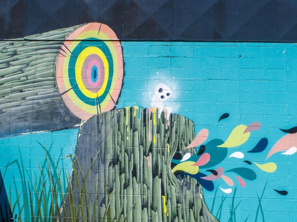 Mural illustration of tree cut at base, showing rainbow rings and various colors of stylized droplets coming out of the stump