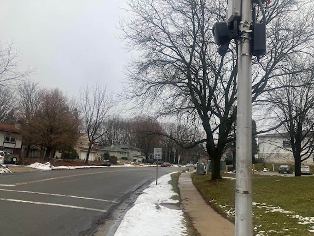 A Flock camera is attached to a pole on a city street. Snow is on the ground.