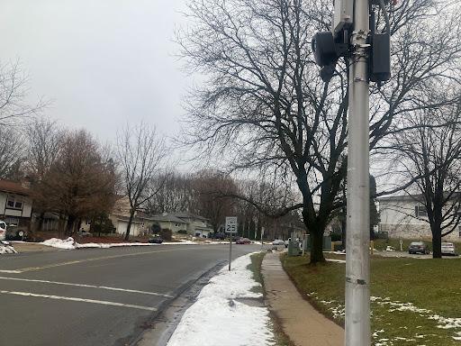 A Flock camera is attached to a pole on a city street. Snow is on the ground.