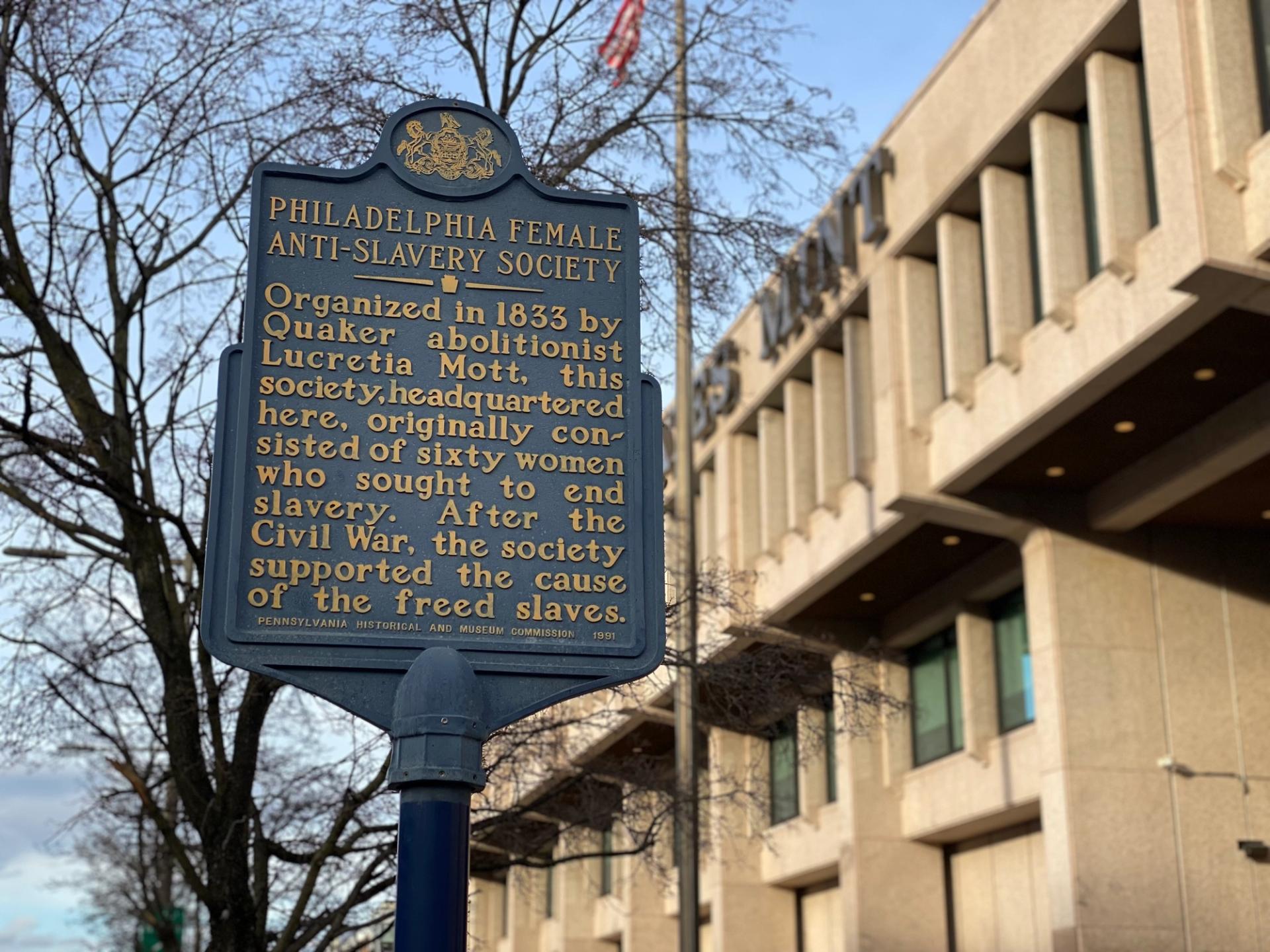 A blue Pennsylvania historic marker that reads: "PHILADELPHIA FEMALE ANTI-SLAVERY SOCIETY. Organized in 1833 by Quaker abolitionist Lucretia Mott, this society, headquartered here, originally consisted of sixty women who sought to end slavery. After the Civil War, the society supported the cause of the freed slaves."