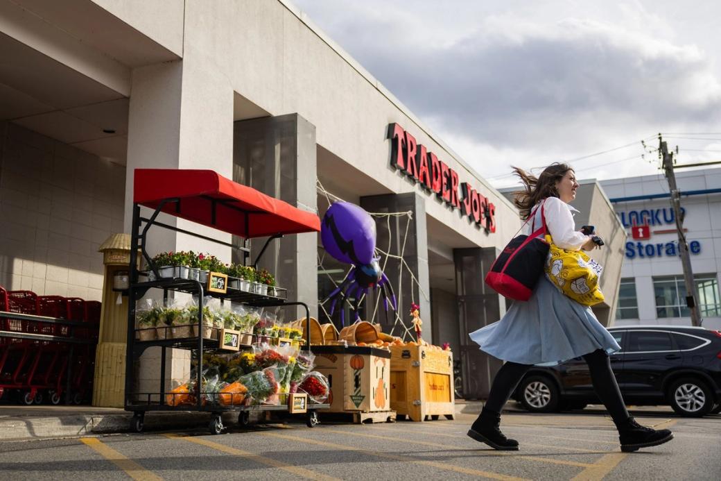 A woman walking out of a Trader Joes with bags in hand