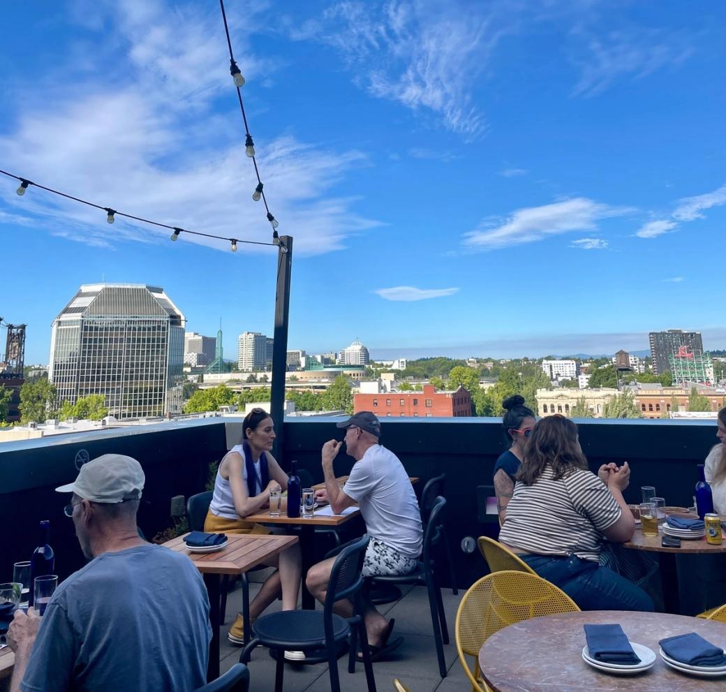 Small groups of people sitting at tables at a rooftop bar on a sunny day.