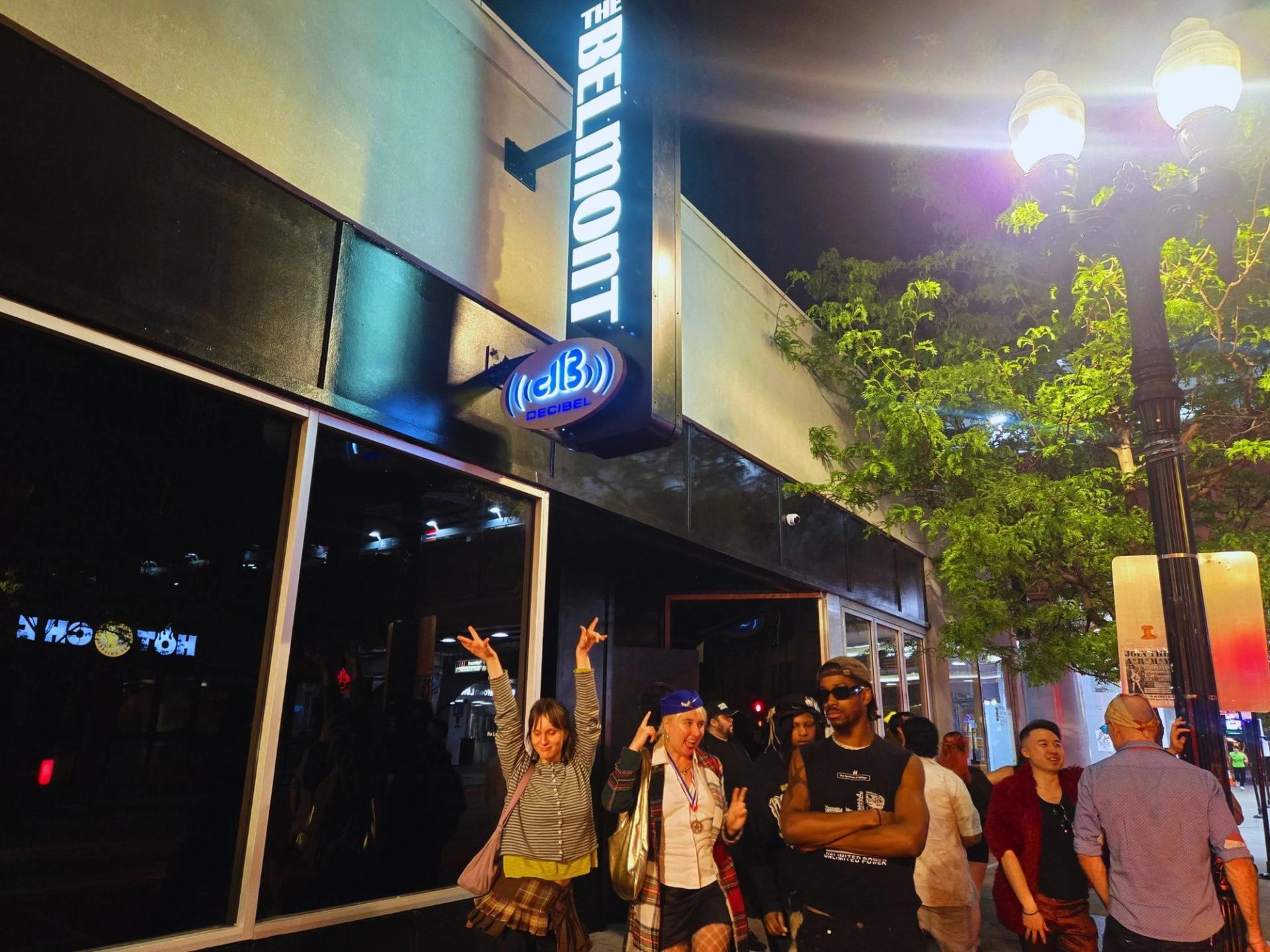 People standing outside of a bar. The sign reads "The Belmont dB"