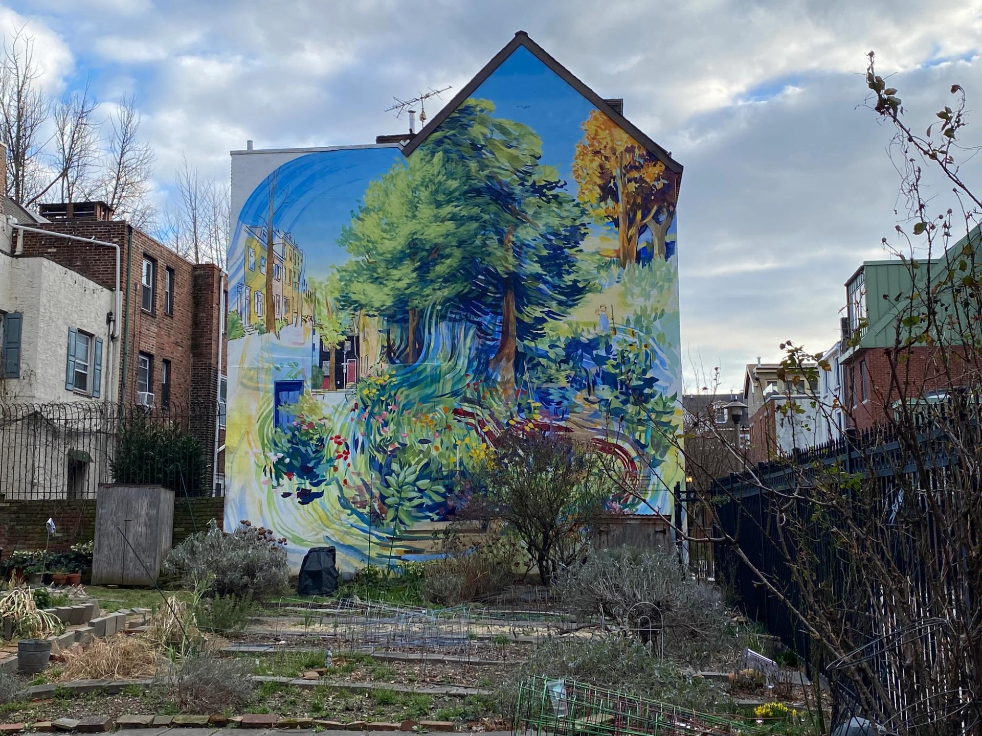 A mural with several trees on the side of a building in front of a garden.