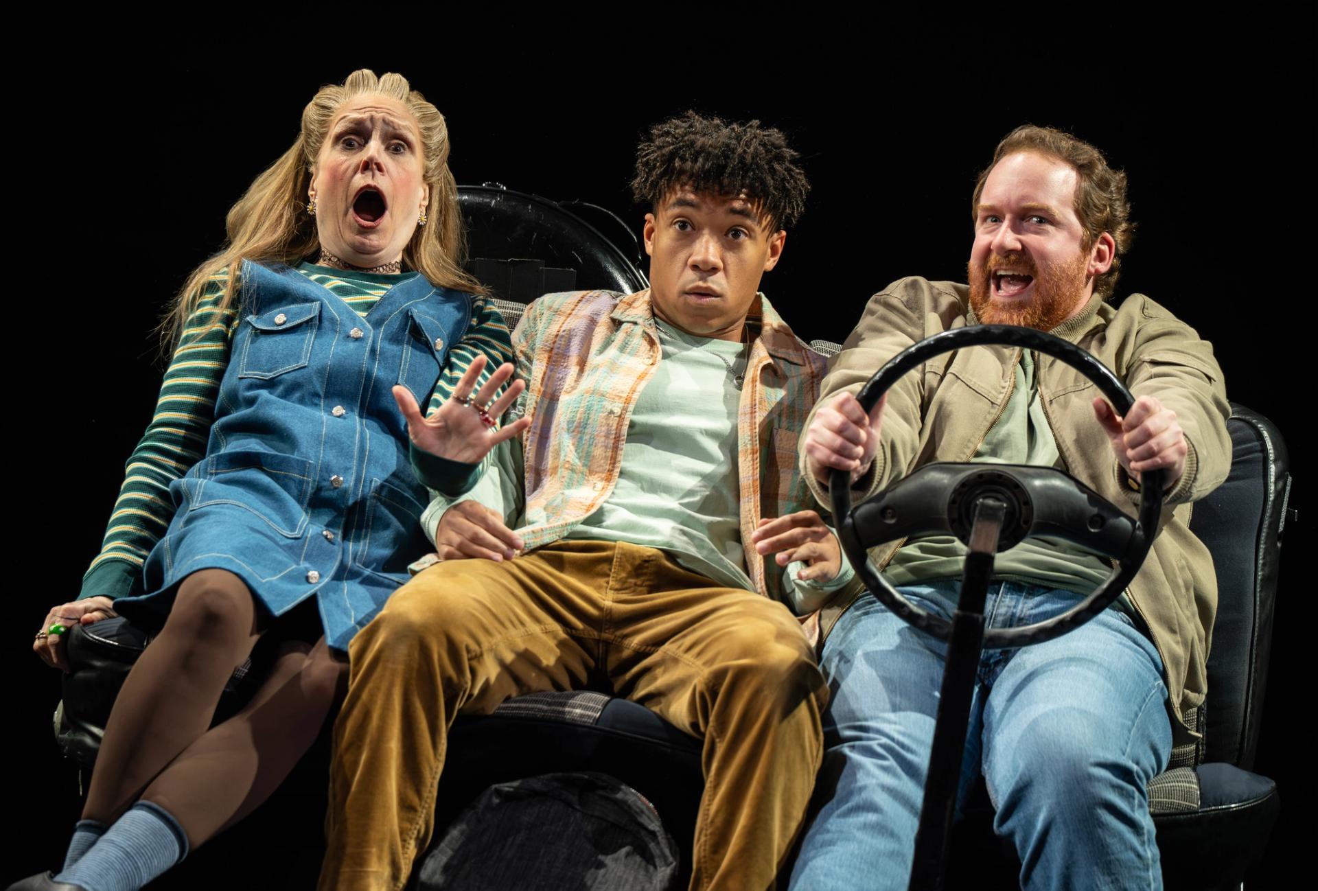 Three people on stage pretending to be riding in a car.