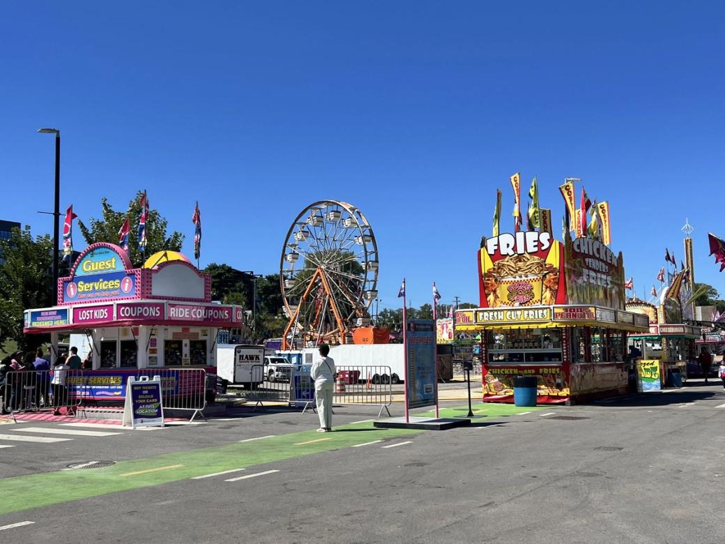 A scene from a fair, with concession stands, a Ferris Wheel, and a ticket booth.