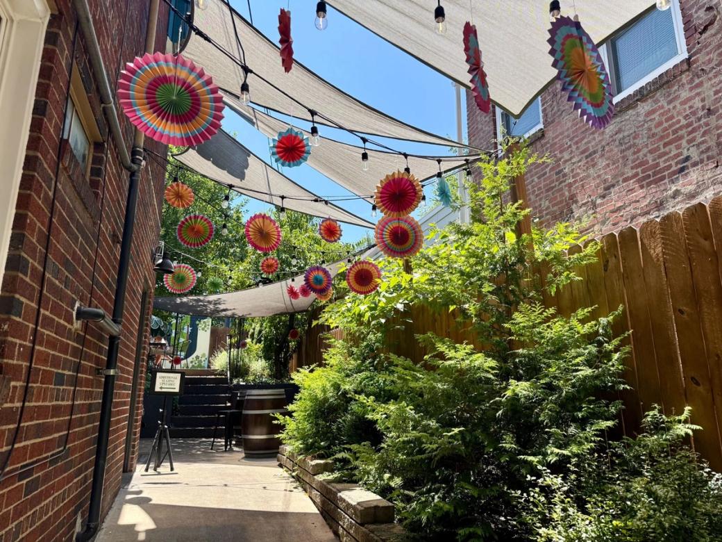 A building’s side patio is shaded with fabric and hanging colored paper fans.