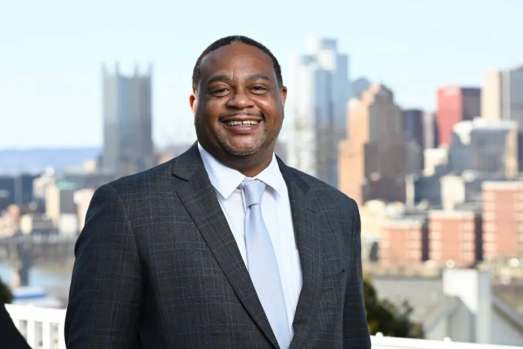 a man in a suit stands in front of pittsburgh's skyline