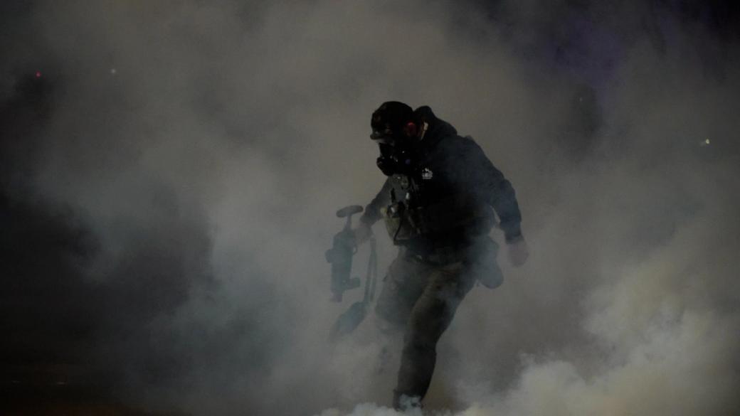 An ICE agent kicks a tear gas canister in a cloud of smoke 