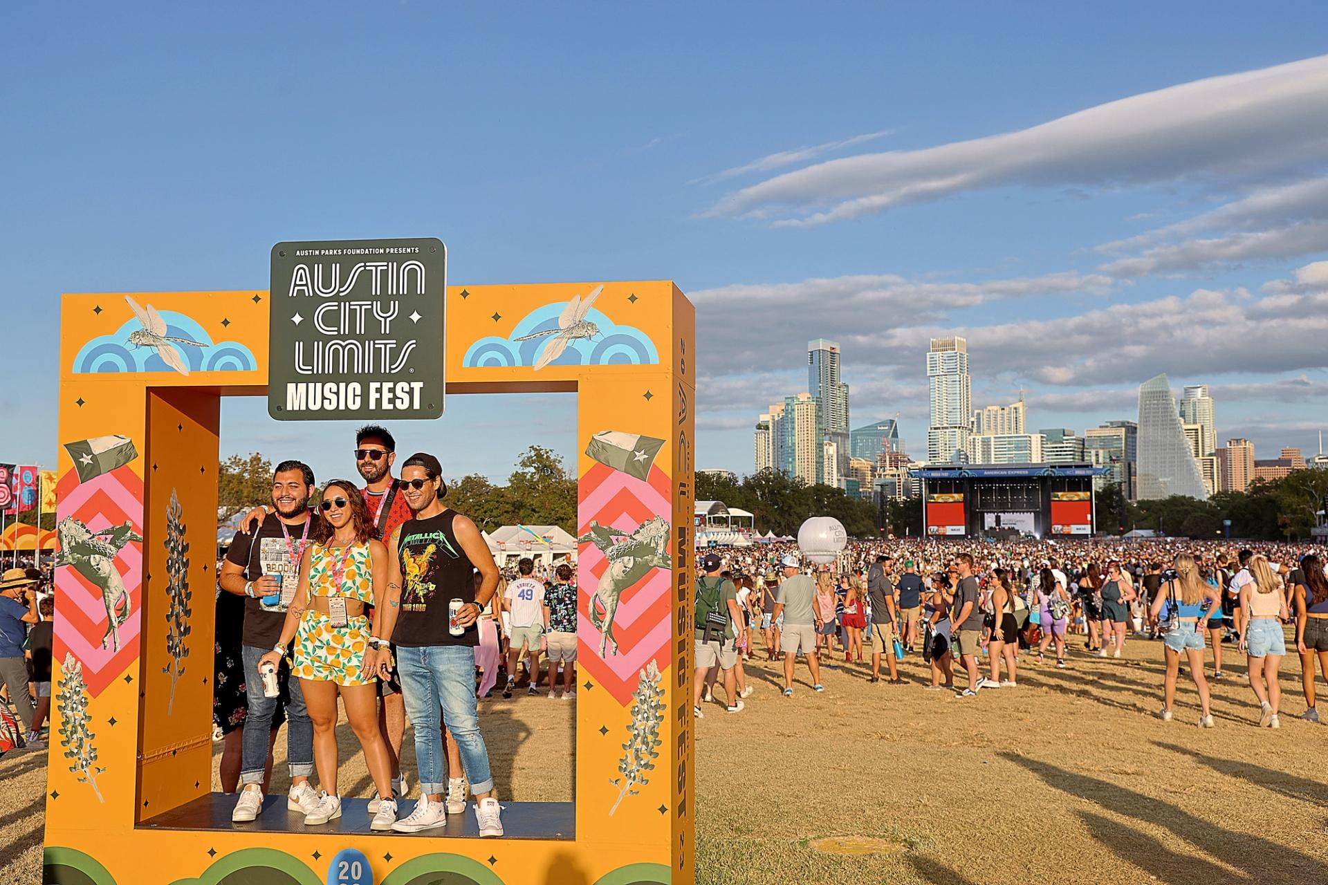 Four people stand in a life size frame that reads "Austin City Limits Music Fest" in Zilker Park with hundreds of people behind them.